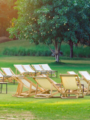 Many empty white deck chairs with tables in lawn is surrounded by shady green grass. Comfortable on outdoor patio chairs in garden.  Lawn chairs in the park. Sunbeds in the garden. Selective focus.