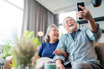happiness asian old senior retired couple enjoy videocall to family together on sofa in living room at home,asian people use smartphone communication to family home isolation ides concept