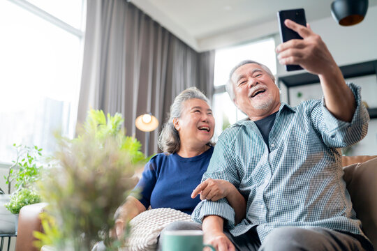 happiness asian old senior retired couple enjoy videocall to family together on sofa in living room at home,asian people use smartphone communication to family home isolation ides concept