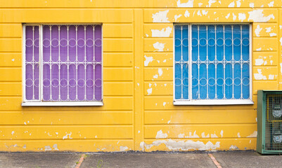 two windows with blue and purple curtains with yellow wall