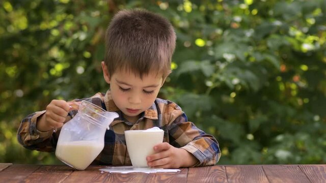 little boy pouring milk into glass and spill it on the table