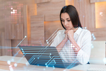Attractive businesswoman in white shirt at workplace working with laptop to optimize development by implying new technologies in business process. Hi tech hologram over office background