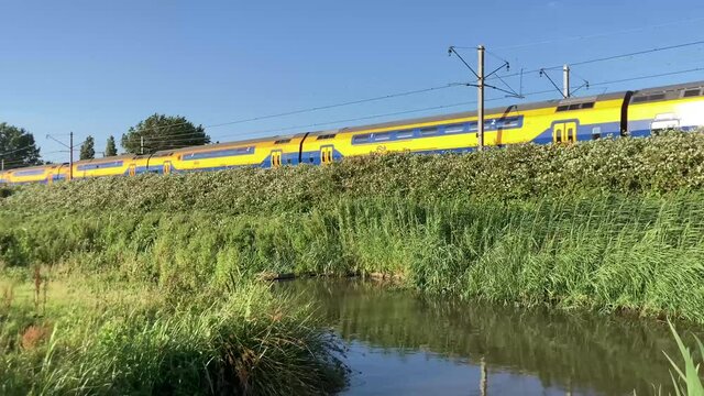 LEIDEN, NETHERLANDS - Aug 07, 2021: A Dutch electric NS passenger train passing green nature reserve in Leiden, The Netherlands