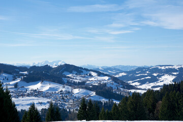 OBERSTAUFEN, GERMANY - 29 DEC, 2017: Wonderful view of the snow-covered winter sports resort of Oberstaufen in the Bavarian Alps with green coniferous trees in the foreground