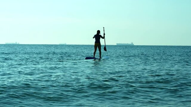 An attractive young woman in a swimsuit paddled a SUP board during the sunrise. Summer, travel, sports, surfing on the board.