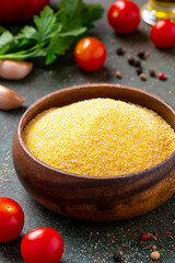 Dry uncooked polenta in a wooden bowl and various ingredients for cooking on a dark table. Traditional Italian food, vegan and healthy food.