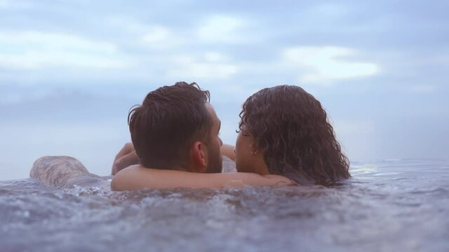 Couple Cuddling and Kissing While Bathing in Infinity Pool With Blue Skies