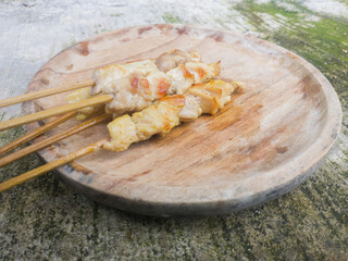 Grilled chicken satay served on a wooden plate