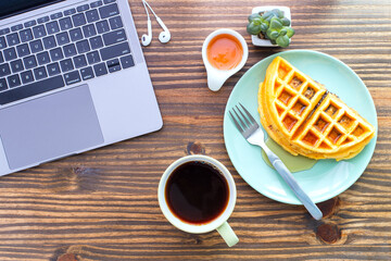 Top table view flat lay on a desk with a laptop computer, cup of coffee and Waffle on green plate with honey cup and cell phone earbuds. Concept of morning working with easy breakfast, ready to work. - Powered by Adobe