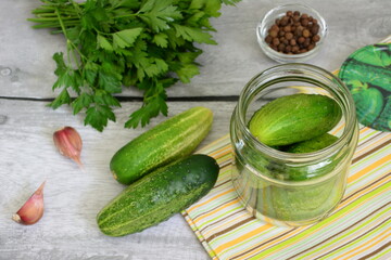 preserving cucumbers in jar for winter with parsley, garlic and allspice on gray wooden background with yellow towel