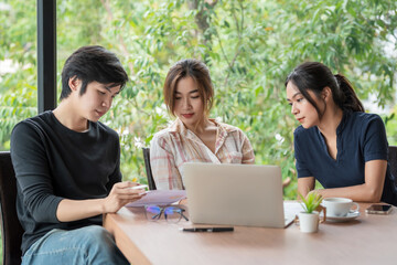 Team of young Asian business people are working together brainstorming discussing together using document and laptop placed at the office.