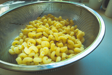 Yellow pasta in an aluminum colander on the table