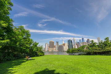 Lawn of the Brooklyn Bridge Park amidst Pandemic of COVID-19 on June 20, 2021 in New York City, USA. Lower Manhattan skyscraper stands beyond the East River.
