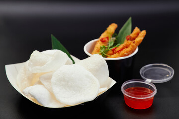 Krupuk or Chinese traditional chips with sauce and shrimps in tempura on black background. Junk food or fastfood concept. Rice chips with sweet and sour or spicy chili sauce. High quality photo