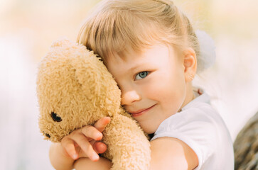 Little girl blonde hugs a soft toy bear