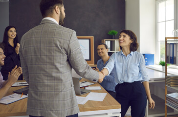Two happy people shaking hands in business meeting as form of praise and recognition. Coworkers applauding as marketing director congratulates employee with getting contract and making successful deal
