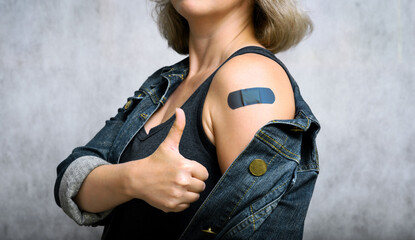 COVID-19 vaccinated young woman showing arm with plaster, vaccine concept