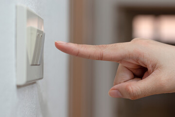 The hand of a woman pressing the light switch on the white wall