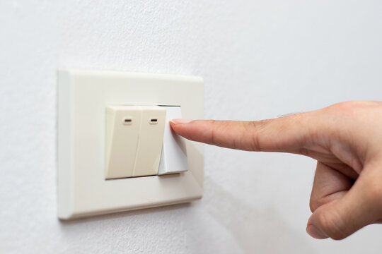 The hand of a woman pressing the light switch on the white wall.