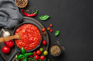 Classic Italian tomato sauce with basil on a black background with ingredients.