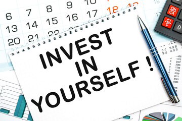Notebook with the text INVEST IN YOURSELF on the office table, documents, calculator, glasses and pen