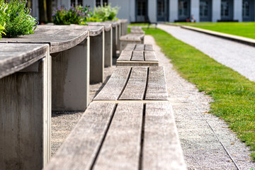 Benches and tables with flowers arranged in a row in the park, in the background a large building with arched windows.