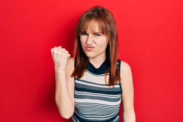 Redhead young woman wearing casual t shirt angry and mad raising fist frustrated and furious while shouting with anger. rage and aggressive concept.