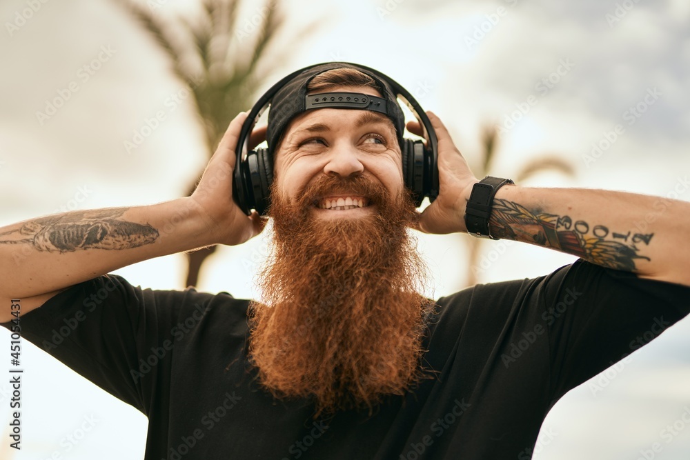 Sticker young irish hipster man smiling happy listening to music using headphones at the city.