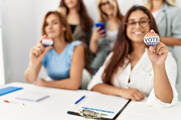 Group of young voter woman smiling happy wearing vote badge sitting on the table at electoral...