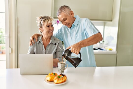 Senior caucasian couple having breakfast using laptop at the kitchen.