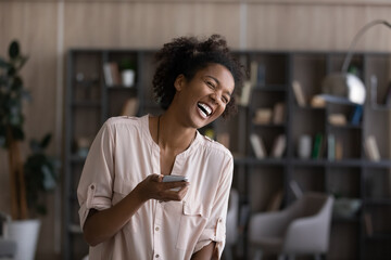 Overjoyed millennial African American woman laugh read good funny news online on smartphone....