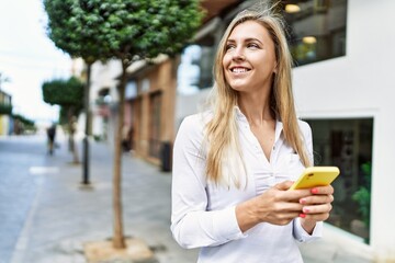 Beautiful blonde woman smiling happy outdoors on a sunny day using smartphone