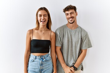 Young beautiful couple standing together over isolated background winking looking at the camera with sexy expression, cheerful and happy face.