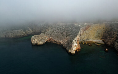 Fort of Santo Antonio de Belixe, landscape aerial photo during sunrise, Atlanic ocean coastline with the fortress in Portugal near Sagres, rocky cliffs with visible erosion, fog and clouds