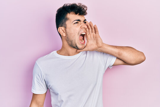 Young hispanic man wearing casual white t shirt shouting and screaming loud to side with hand on mouth. communication concept.