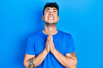 Young hispanic man wearing casual blue t shirt begging and praying with hands together with hope expression on face very emotional and worried. begging.