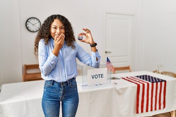 Beautiful hispanic woman standing by at political campaign by voting ballot laughing and...