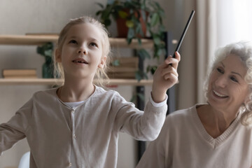 Small teen girl child have fun study together with old Caucasian grandmother at home. Little...