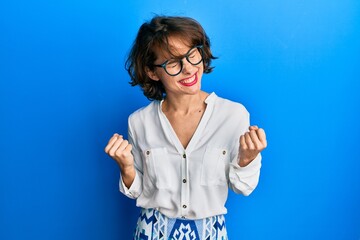 Young brunette woman wearing casual clothes and glasses very happy and excited doing winner gesture with arms raised, smiling and screaming for success. celebration concept.