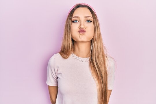 Young blonde girl wearing casual clothes puffing cheeks with funny face. mouth inflated with air, crazy expression.