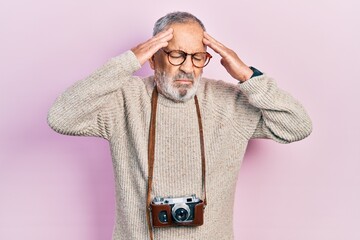 Handsome senior man with beard holding vintage camera with hand on head, headache because stress....