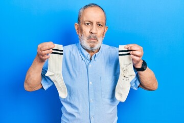 Handsome senior man with beard holding clean andy dirty socks relaxed with serious expression on...
