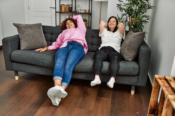 Obraz premium Mature mother and down syndrome daughter at home resting on the sofa