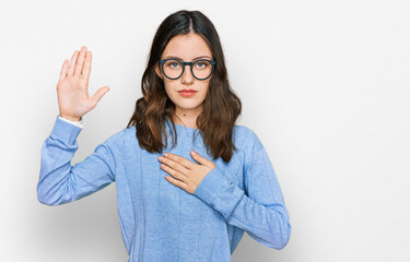 Young beautiful woman wearing casual clothes and glasses swearing with hand on chest and open palm,...