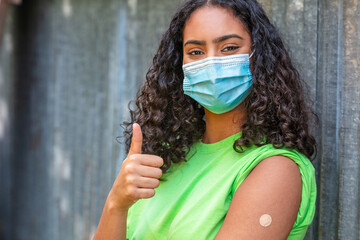 Vaccinated African American female young woman wearing face mask and vaccine band aid