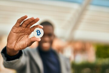Young african american man smiling happy holding bitcoin at the city
