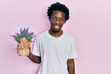 Young african american man holding lavender plant looking positive and happy standing and smiling with a confident smile showing teeth