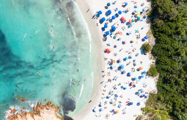 Fototapeta na wymiar View from above, stunning aerial view of a white sand beach full of beach umbrellas and people swimming in a turquoise water. Spiaggia del Principe, Costa Smeralda, Sardinia, Italy.