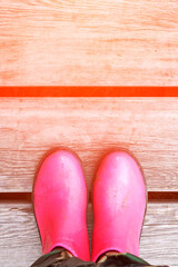 Pink puddle. Rain bright boots. Dirty safety shoes. Summer weather. Walking at mountains. Person feet. Rainy. Wood background