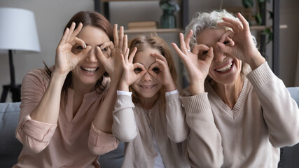 Portrait of happy three generations of Caucasian women make glasses spectacles with fingers hands....